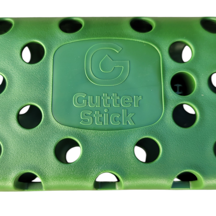 A close-up view of the Gutter Stick’s logo, embossed on the green plastic surface, surrounded by multiple drainage holes that allow for continuous water passage.