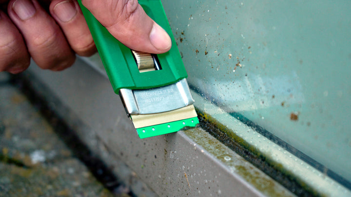 Person using a green window cleaning tool to remove dirt from a glass surface.