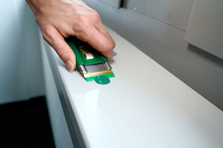Hand using a green utility knife on a white surface
