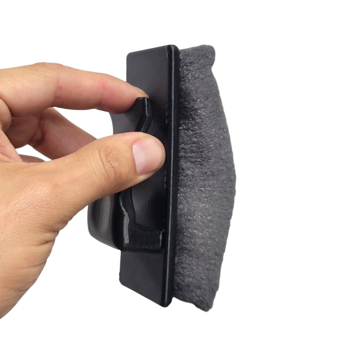 Hand holding a black mag scrubber with a steel wool pad on a white background