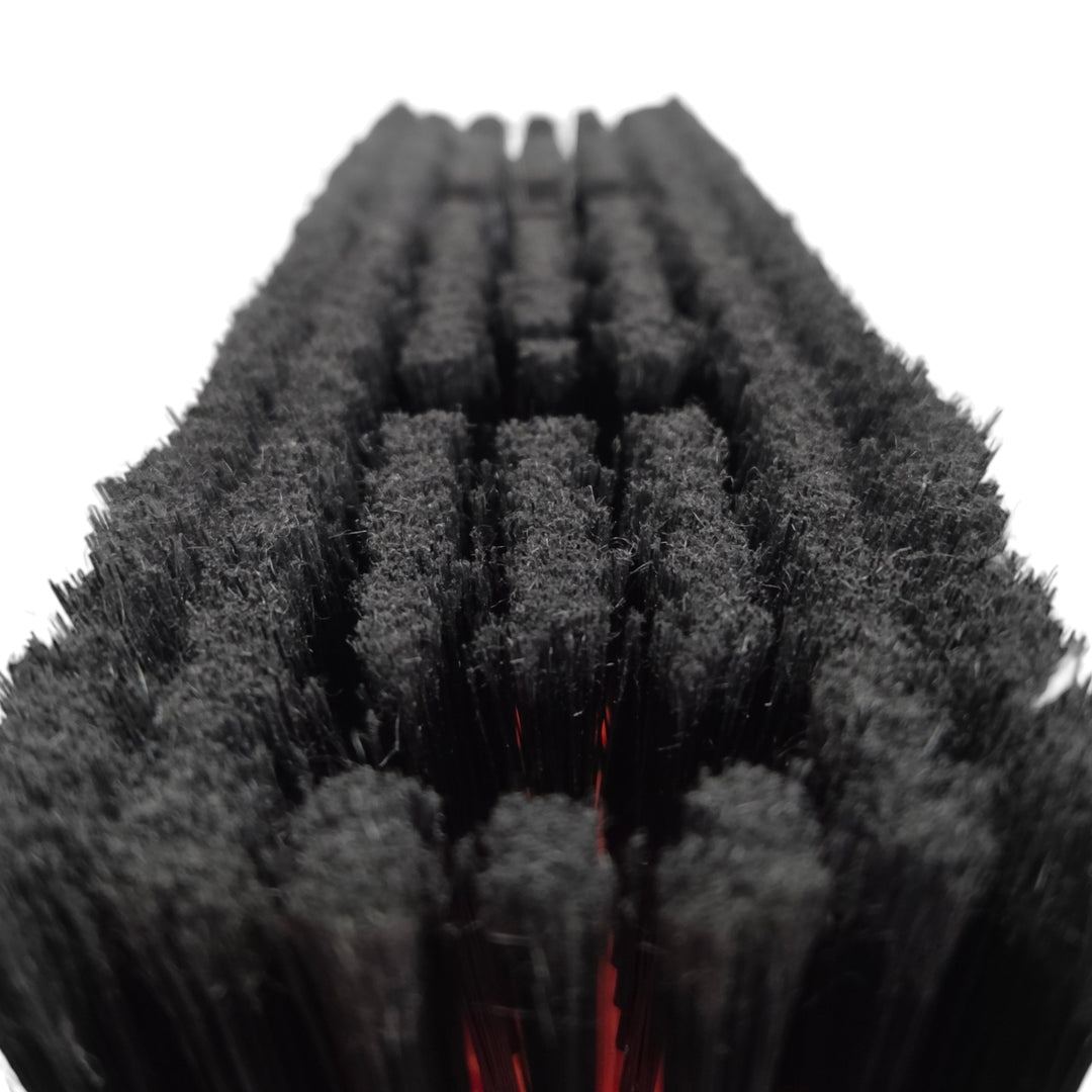 Close-up of a row of black nylon bristle brushes arranged in parallel rows, with a small red accent visible between some bristles, on a white background.