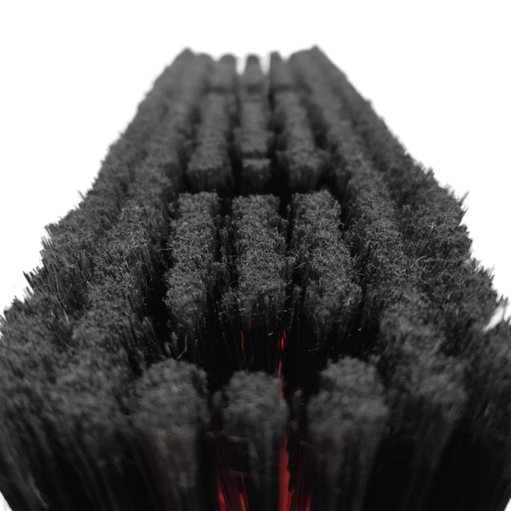 Close-up of a row of black nylon bristle brushes arranged in parallel rows, with a small red accent visible between some bristles, on a white background.