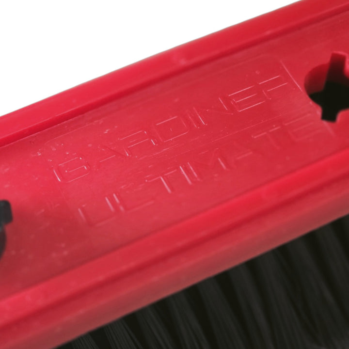 Close-up of a red plastic brush with embossed branding and black bristles visible along the bottom edge.