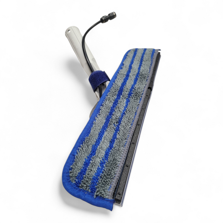 Close-up view of the Wagtail Jetstream cleaning tool showing the dual-material microfiber pad with blue and gray scrubbing stripes, attached to a lightweight handle with a connected water hose.