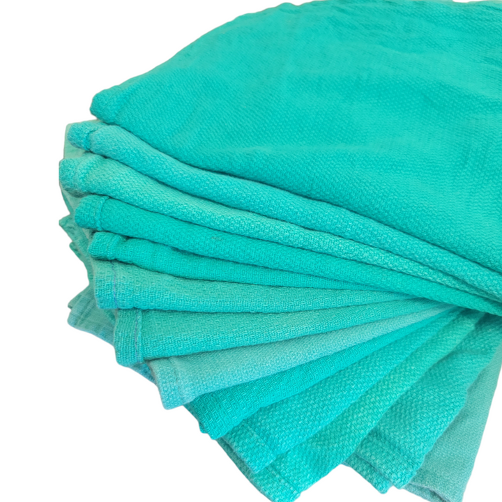 A stack of teal reclaimed surgical towels neatly arranged and fanned out on a white background, highlighting the uniform size and vibrant color.