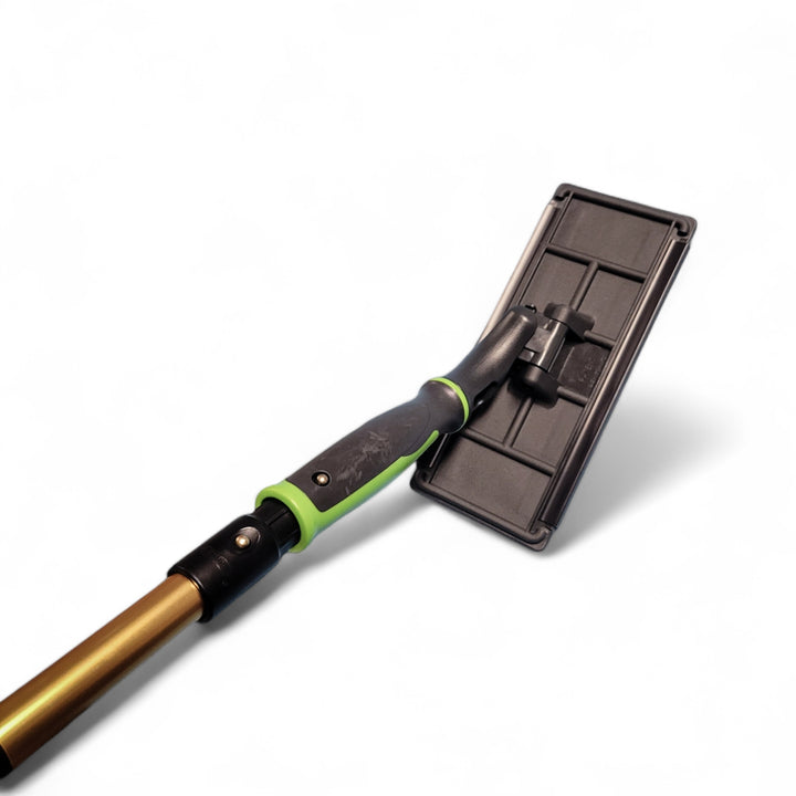 Professional scrubbing tool connected to a golden extension pole, featuring a black pad holder and a green and black ergonomic handle. The joint between the handle and holder is designed to articulate, showcased against a white background.