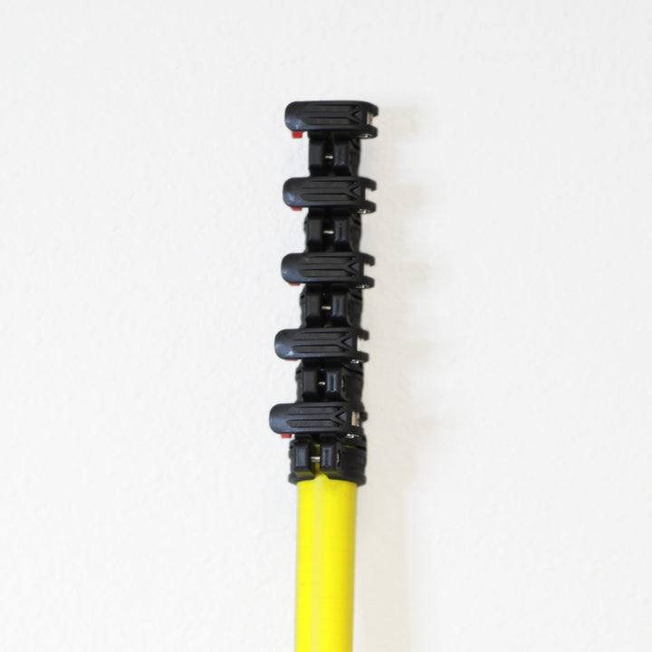 Vertical image of a yellow water fed cleaning pole with multiple black clamping mechanisms against a white wall.