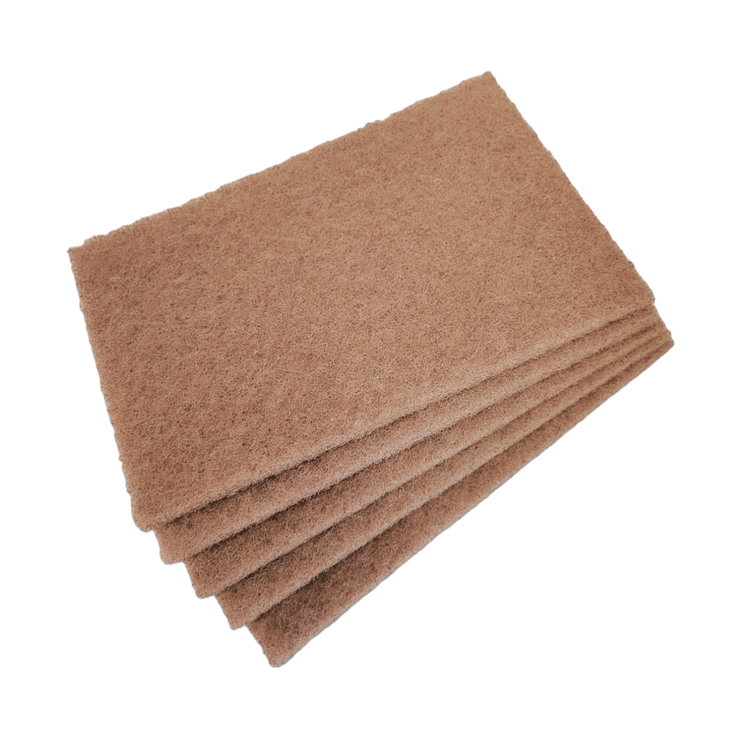 A stack of brown walnut scrub pads neatly piled on top of each other. Each pad is rectangular, showing a consistent, coarse texture, indicative of the natural abrasive material.