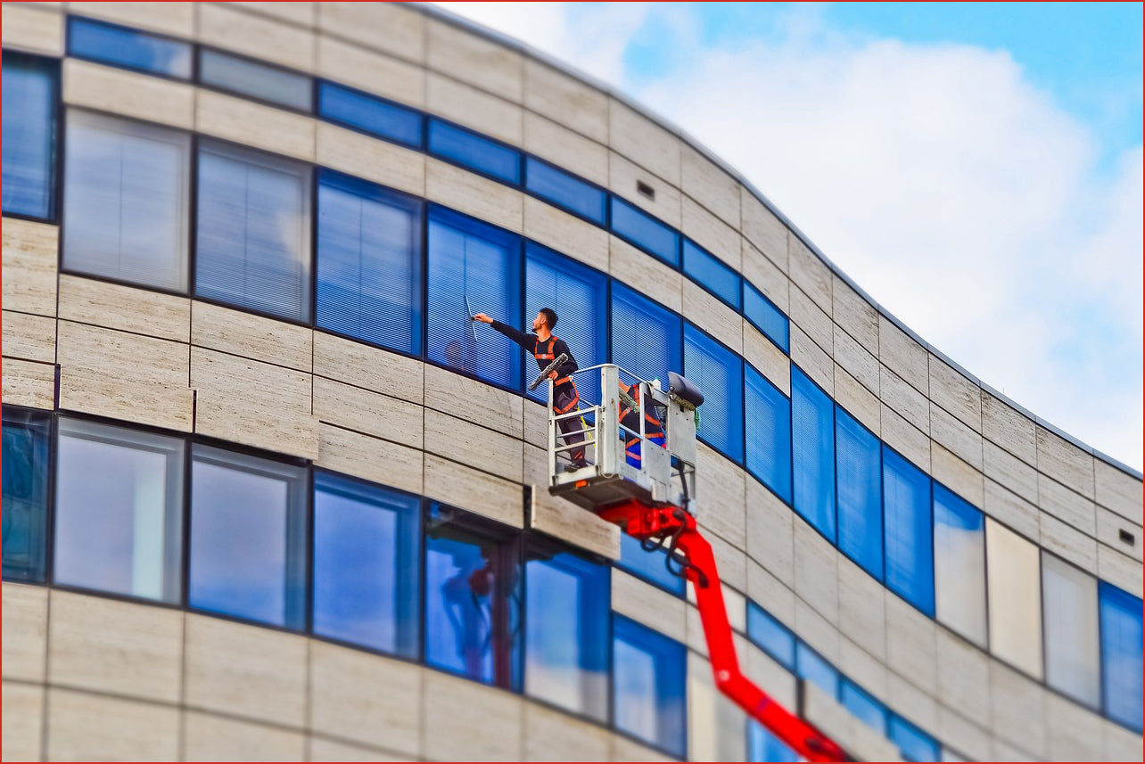 Two men wearing harnesses cleaning windows on a boom lift.