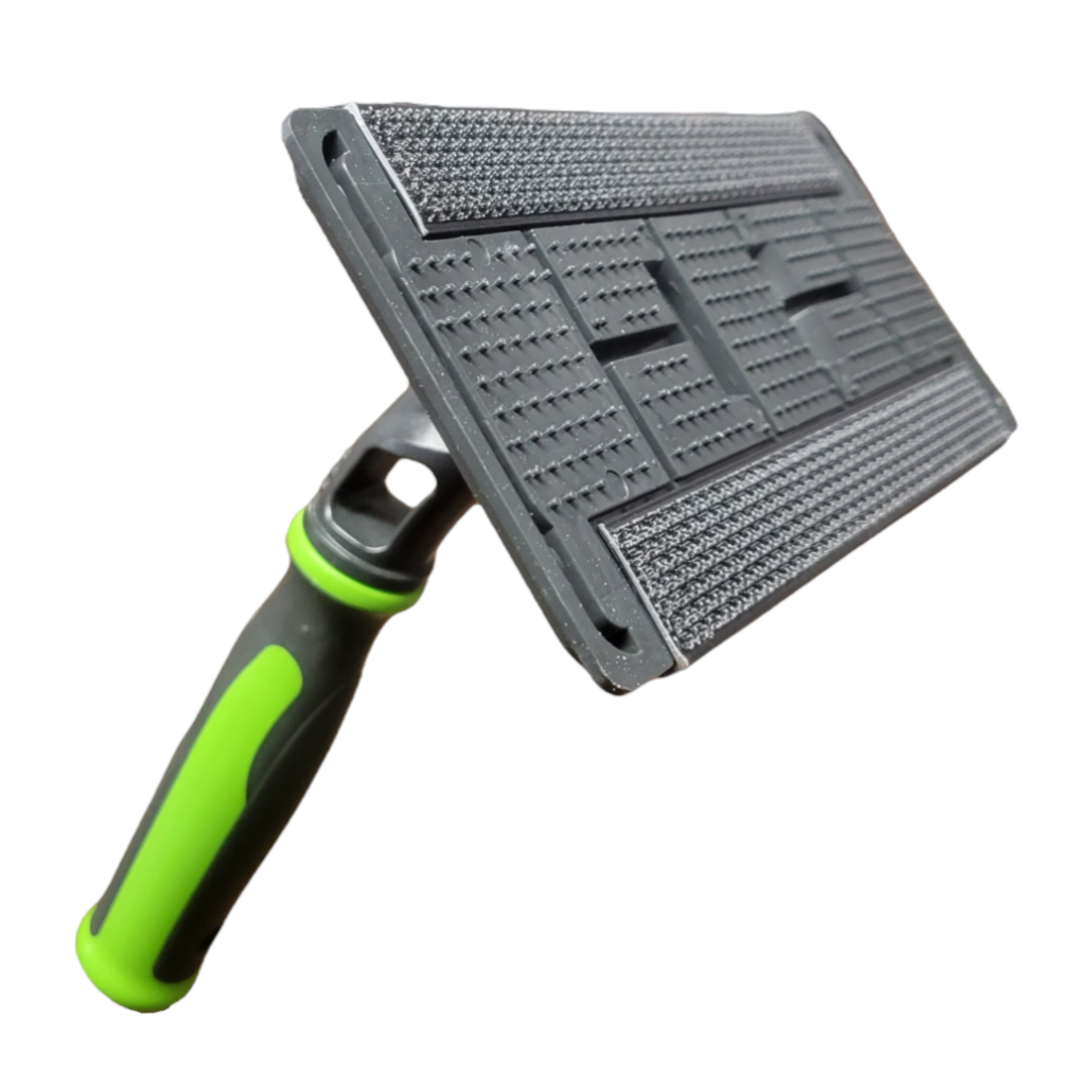 Angled view of a cleaning scrubber tool with a textured gray pad attached to a black holder. The handle, with green accents, shows its ability to pivot, against a white backdrop.